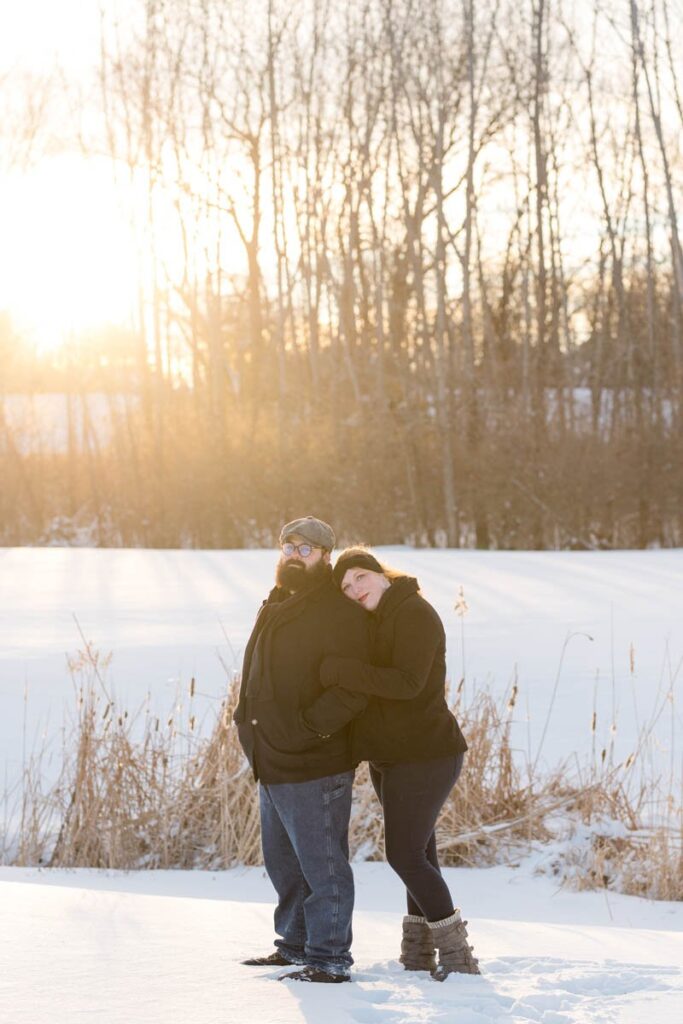 Woman hugs man from behind as they stand seriously in the snow.
