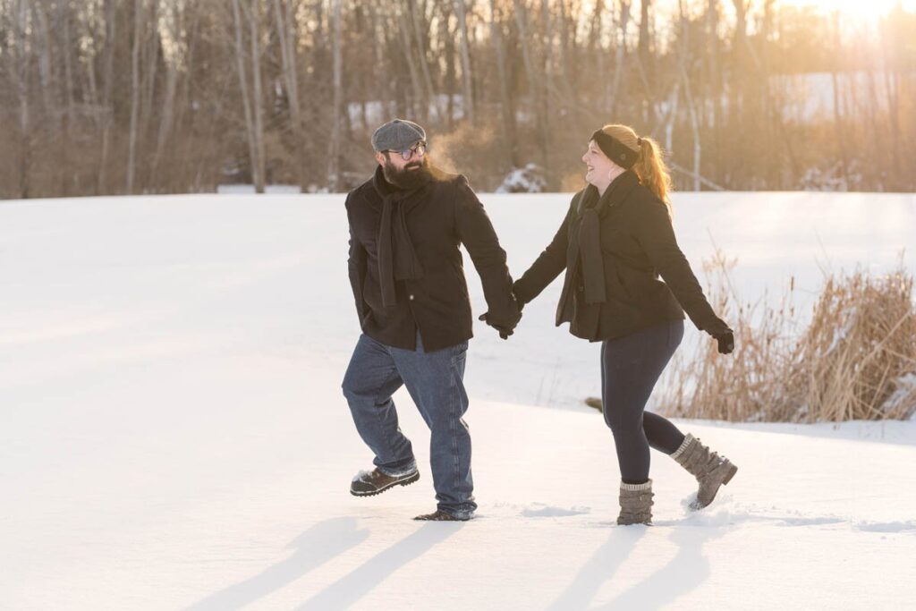 Man leads woman through the snow as the sun sets behind them.