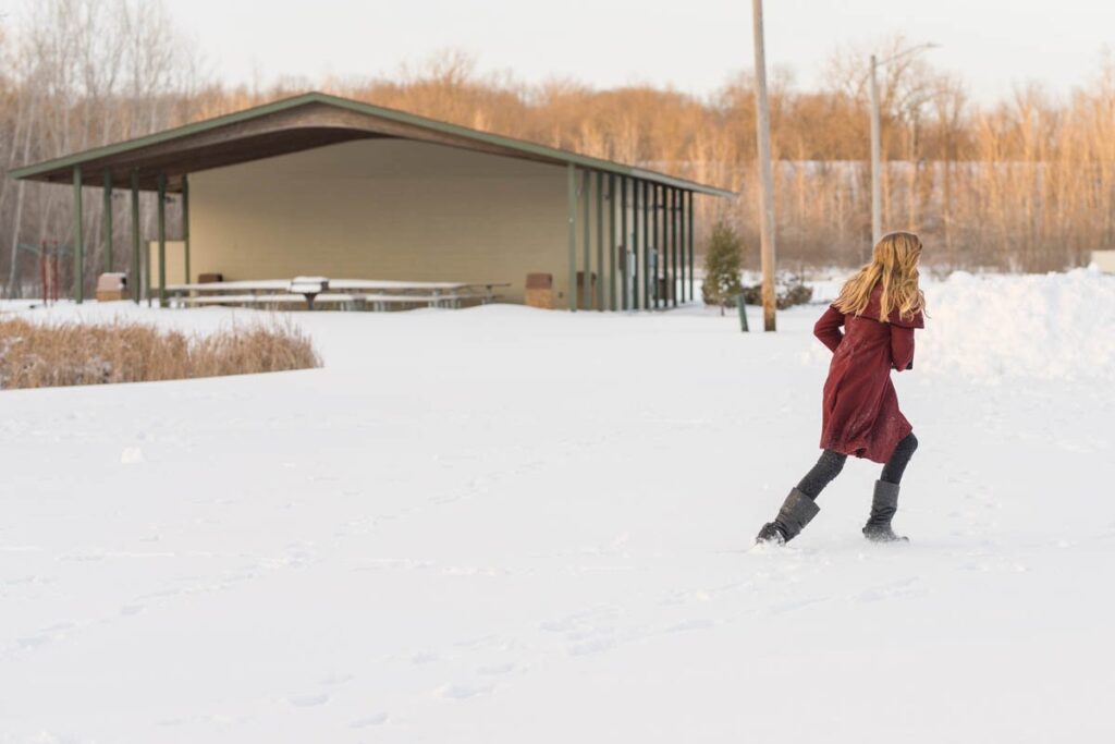 Girl in maroon jacket runs from family snowball fight.