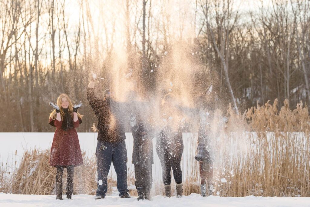 Family throws snow into the air during their photoshoot in the snow.