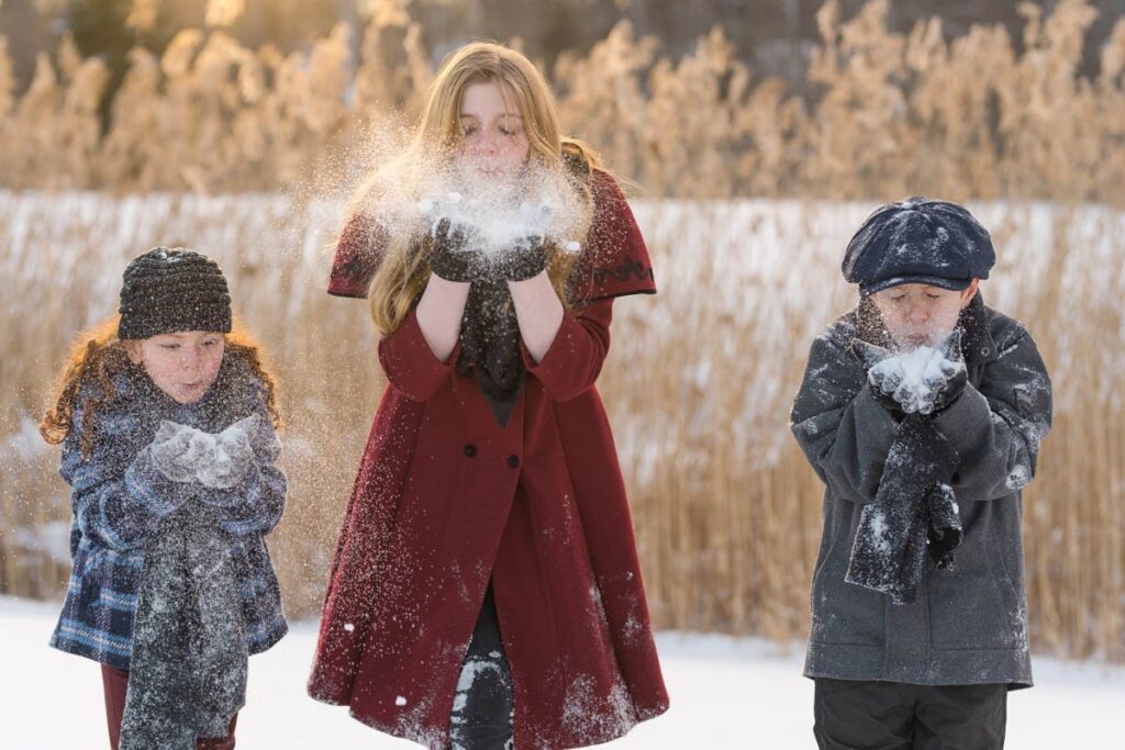 Siblings blow snowy powder during their photoshoot in the snow.