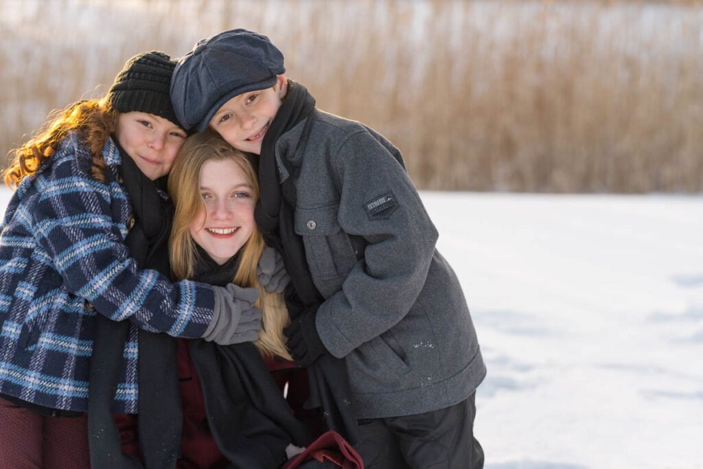 Siblings hugging during their photoshoot in the snow to stay warm.