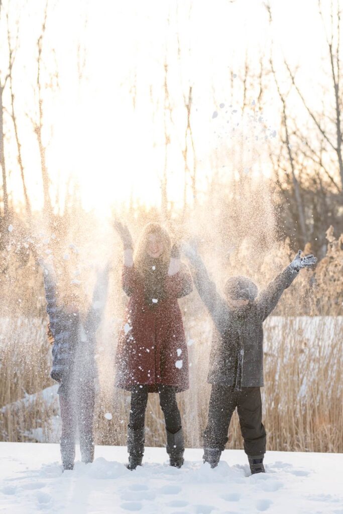 Three kids toss snow in the air with the setting sun behind them.