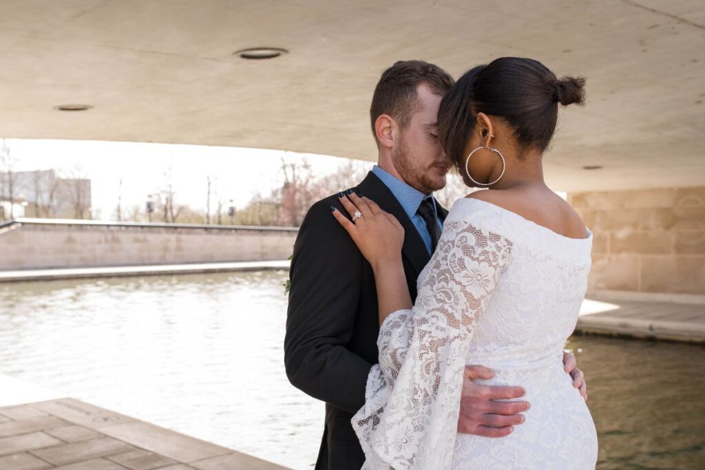 Bride and groom holding one another close with their eyes closed under a bridge with canal next to them.