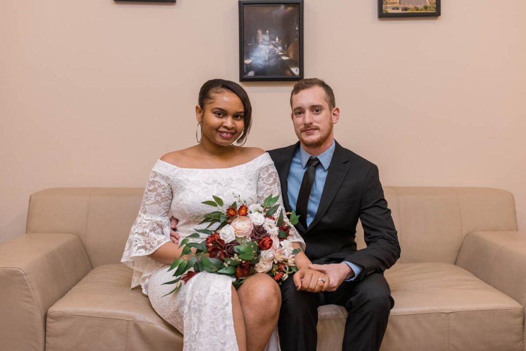 Bride and groom sit on a couch smiling.