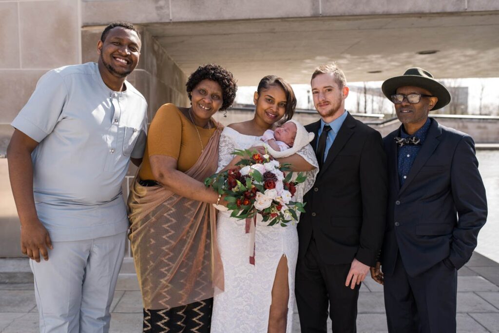 Bride and groom hold their daughter while family gathers around smiling.