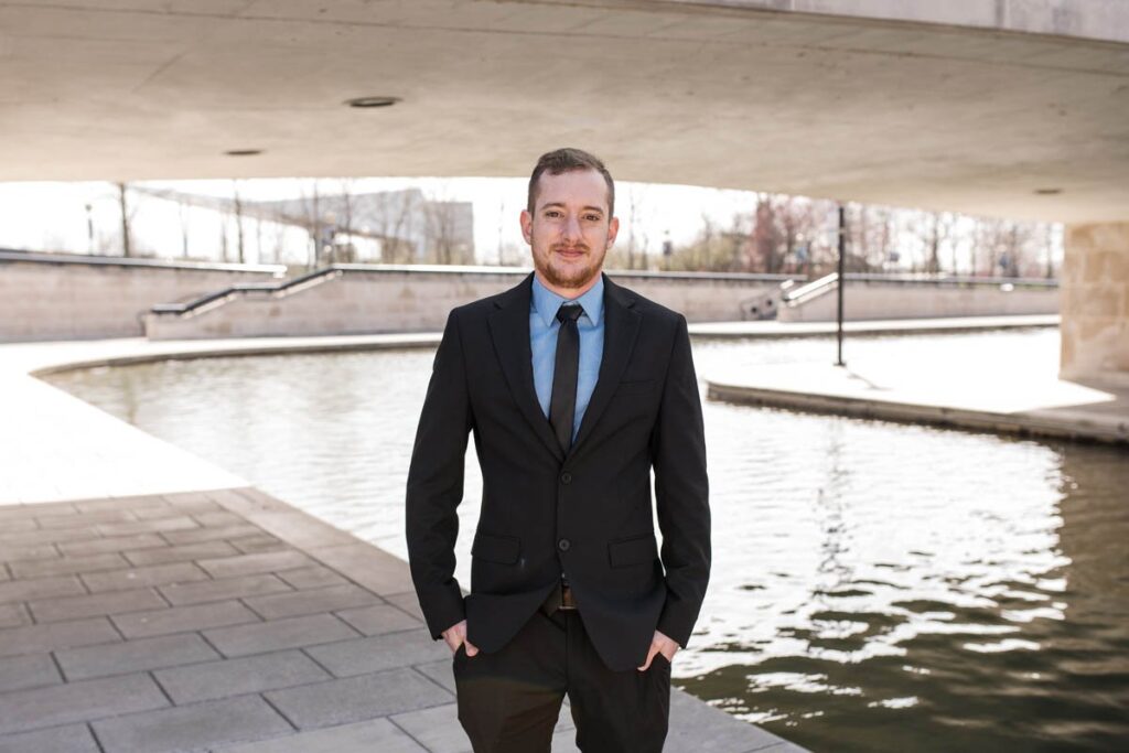 Groom stands with his hands in his pockets under bridge near canal for a portrait.
