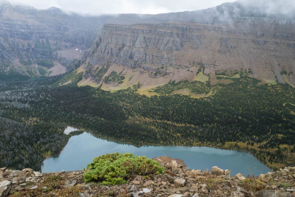 A blue lake is located at the foot of cloud-covered mountains.