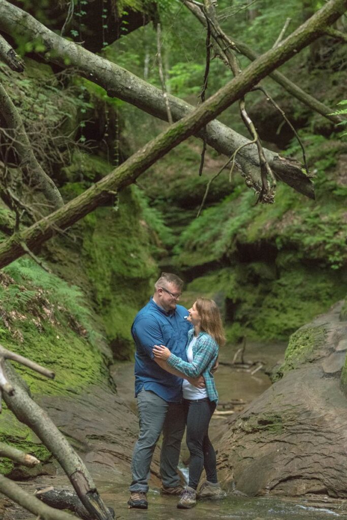 Couples stands on a wet, rocky trail holding one another during their hike.