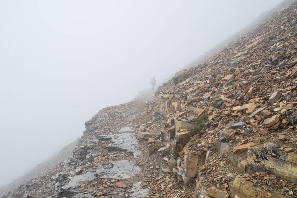 Hiker walking on rocky trail that is covered in dense fog.