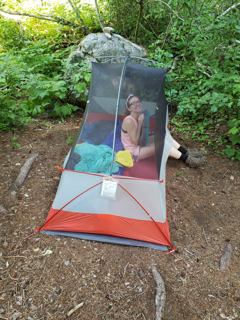 Girl sitting in tent in designated campsite smiling.