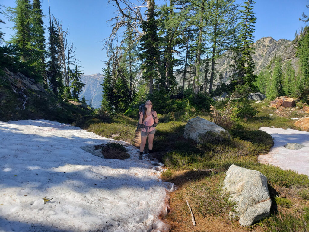 Female hiker sticking to the trail that is partially covered in snow pack on a mountain in North Cascades National Park.