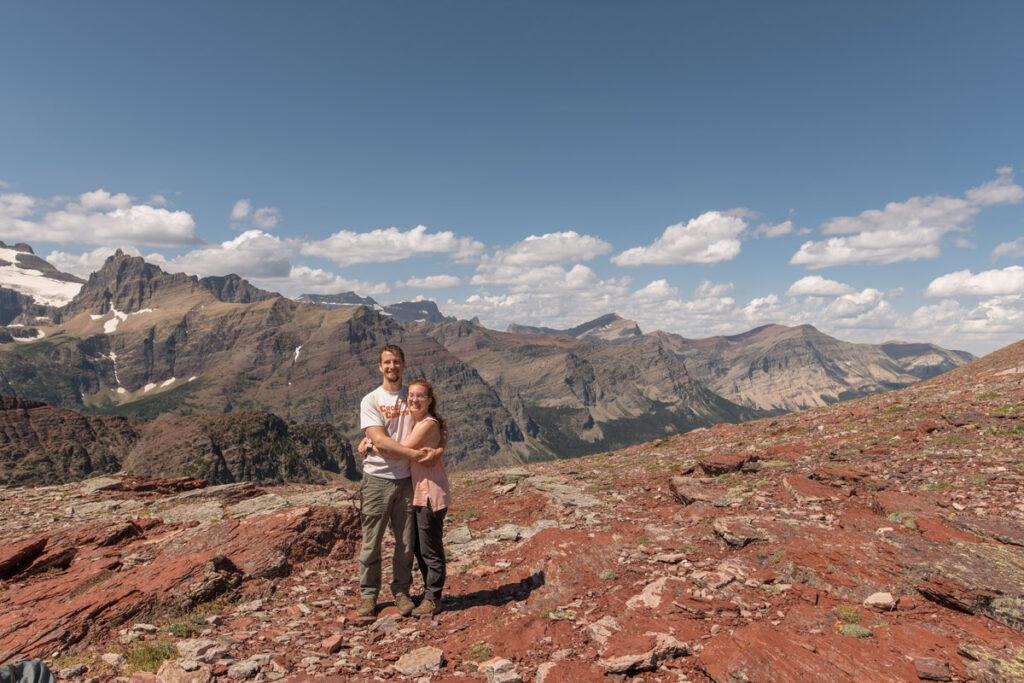 Couple hugs while standing in a red rocky area on top of a mountain range in the backcountry of Glacier National Park.