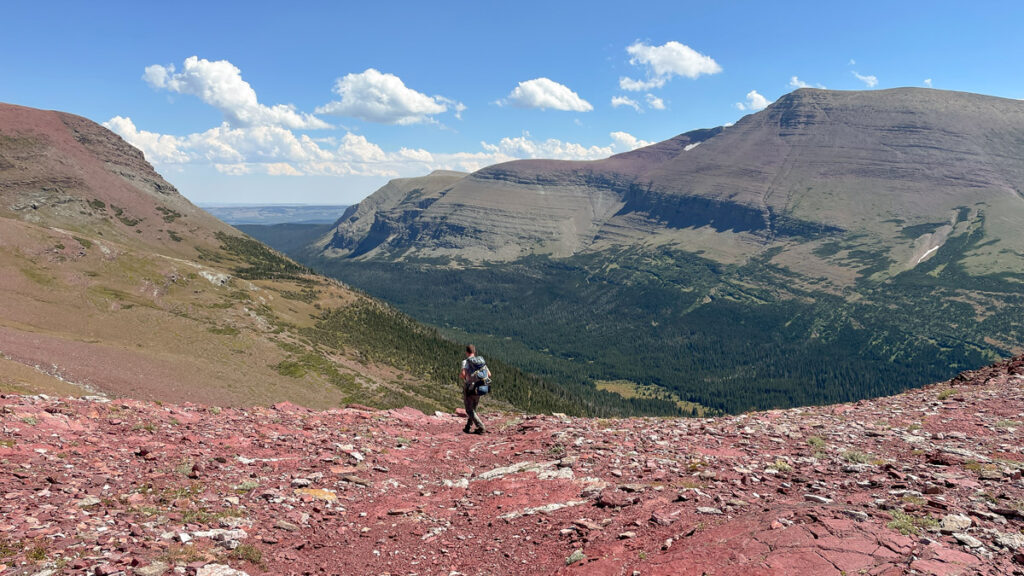 Male hiker on red rocky trail on top of a mountain range in Glacier National Park.