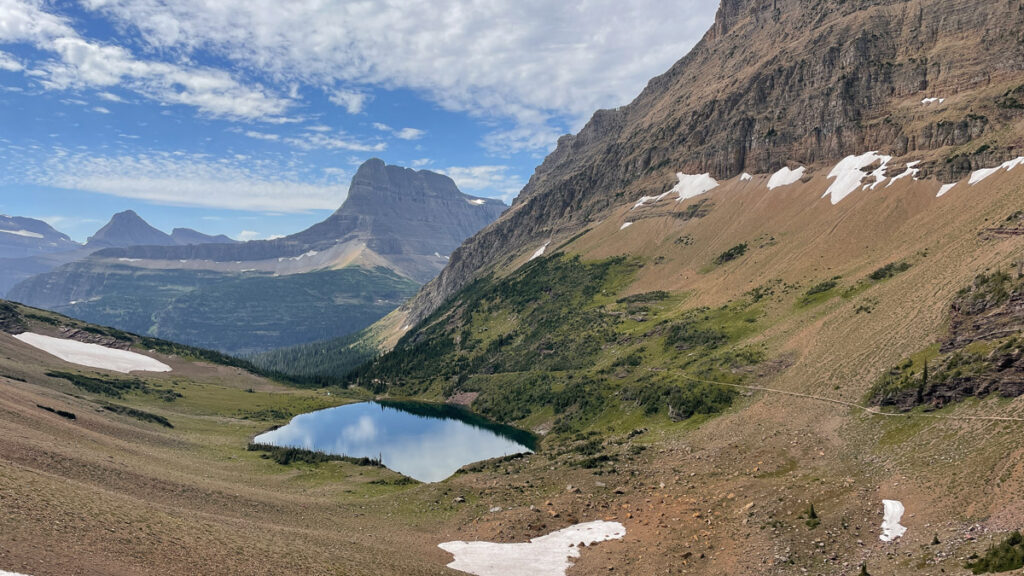 Glacier National Park hiking trail on a sunny day where blue sky is reflected in lake below.