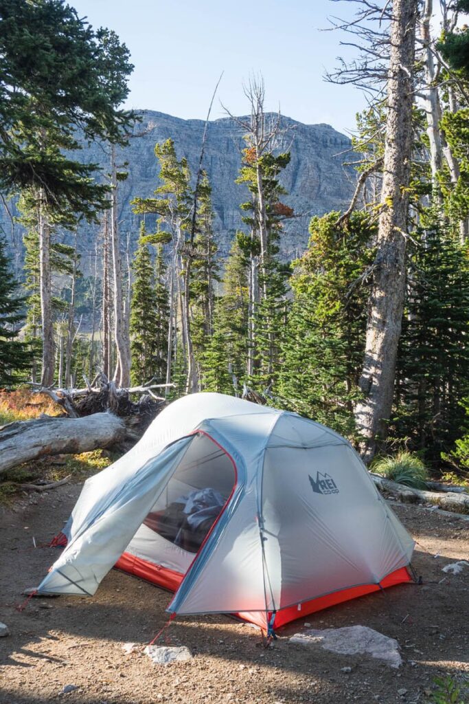 Grey and orange tent sitting on durable surface campsite with mountains and green trees around it.