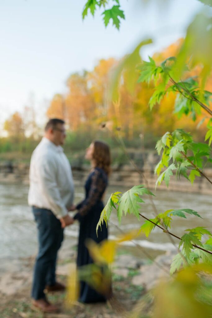 Focus is on leaves in foreground while couple holds hands in the blurry background.