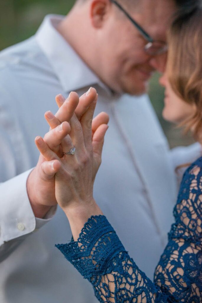 Couple holds hands with interlaced fingers and ring is in focus.
