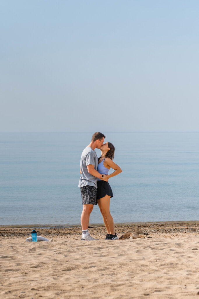 Couple kisses on the beach after woman says yes to proposal.