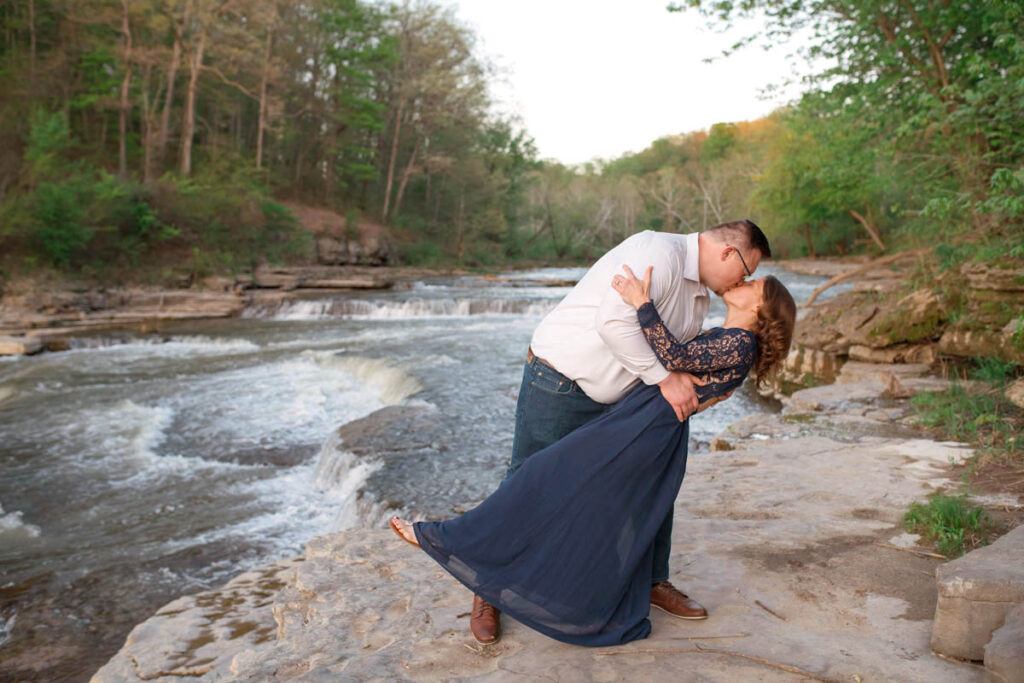 Man dips woman and kisses her in front of a waterfall following surprise proposal.