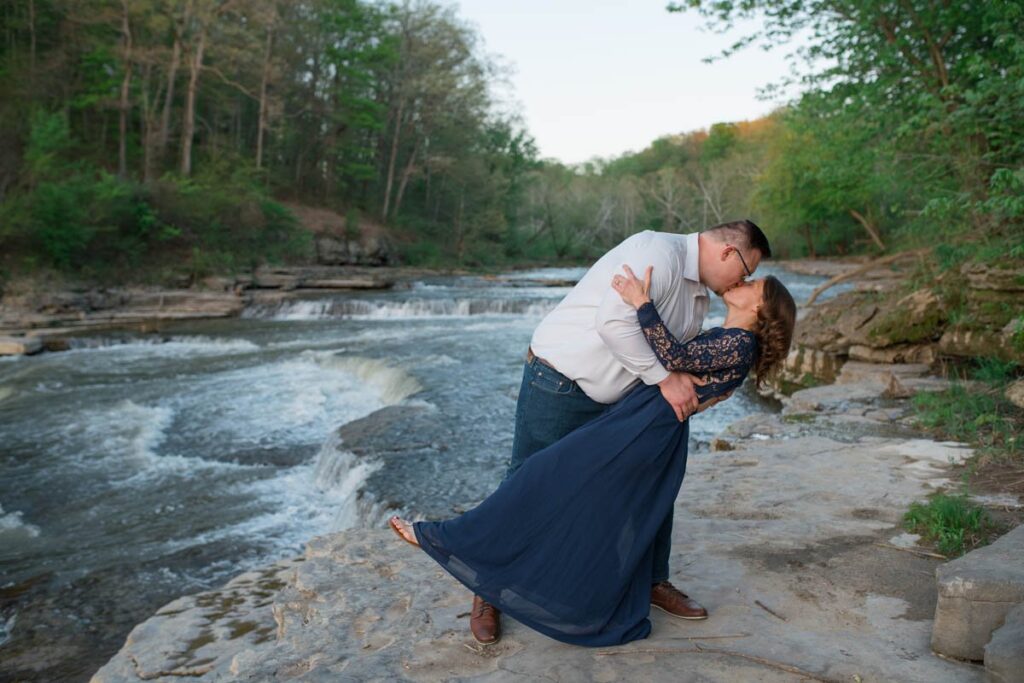 Man dips woman and kisses her in front of a waterfall.