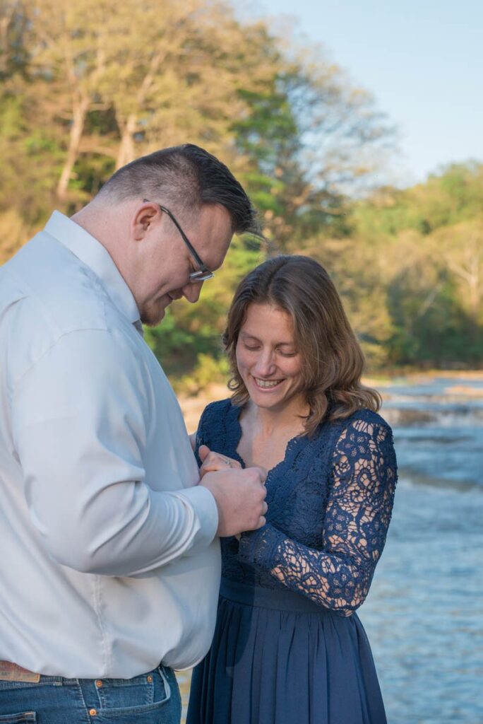 Newly engaged couple looks down at ring on woman's hand while smiling.