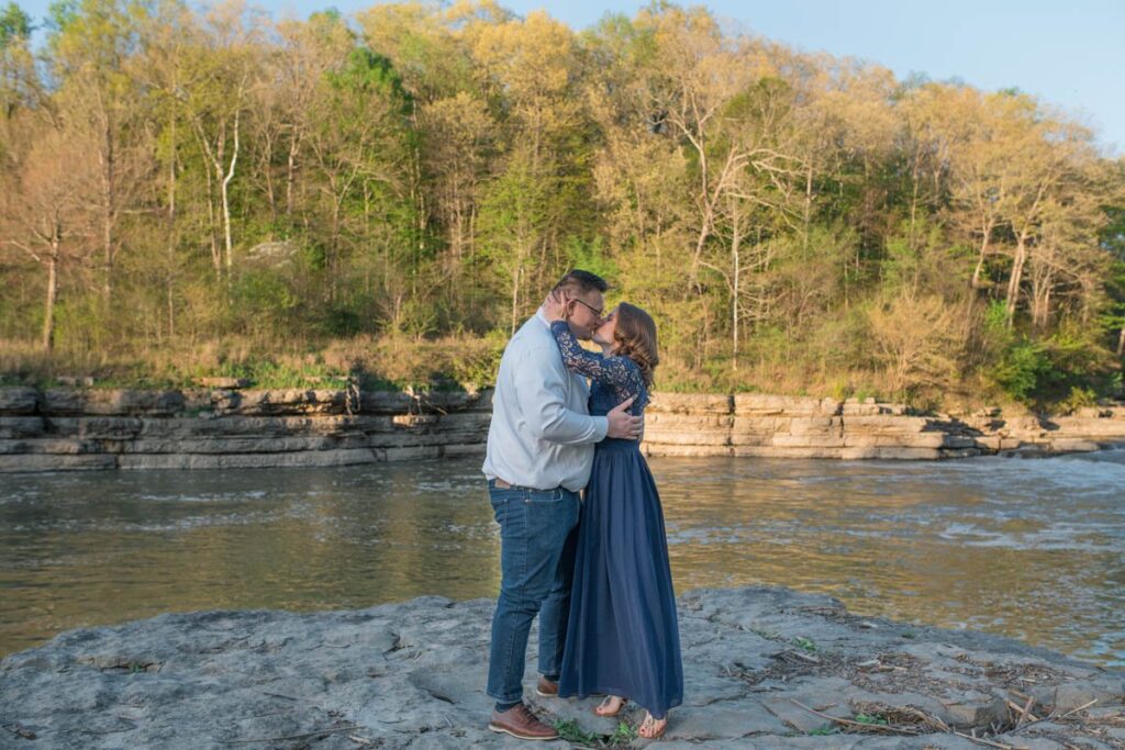 Couple kisses on rock in front of falls after woman says yes to proposal.