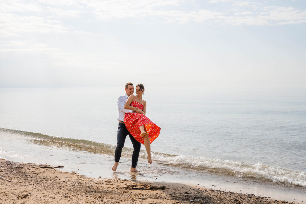 Man sets woman down onto shoreline while they play on the beach.