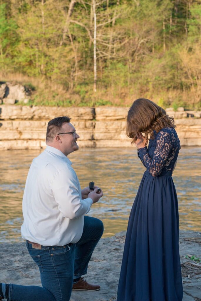 Proposal photographer documents man proposing with ring in box and woman has hands on her face surprised.