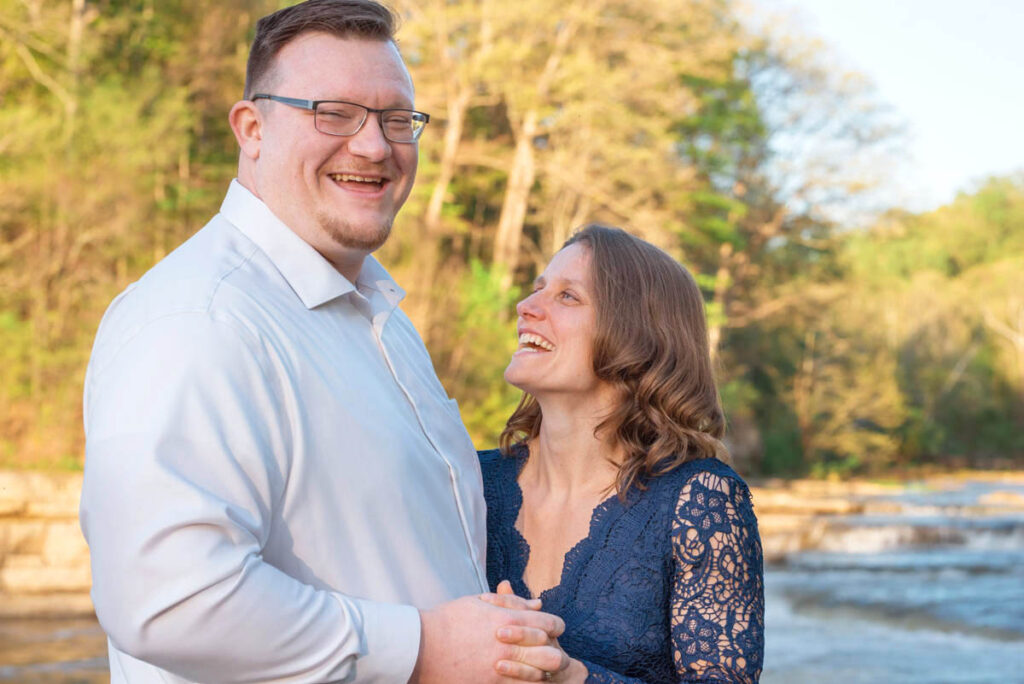 Woman looks up at man smiling while man laughs while looking at proposal photographer.