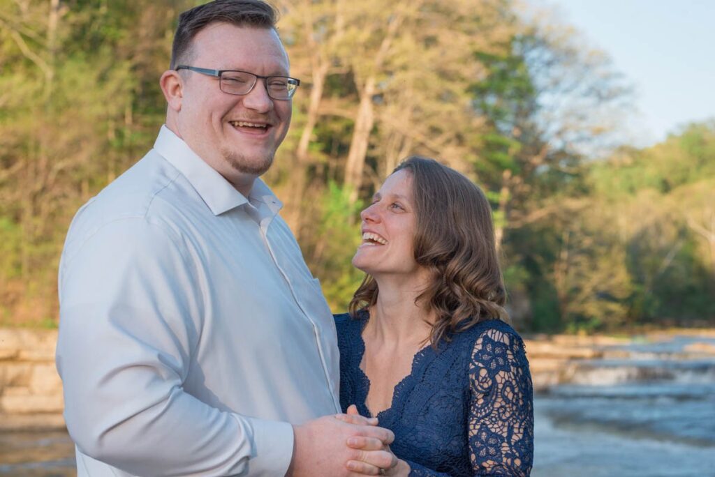Woman looks up at man smiling while man laughs while looking at proposal photographer.