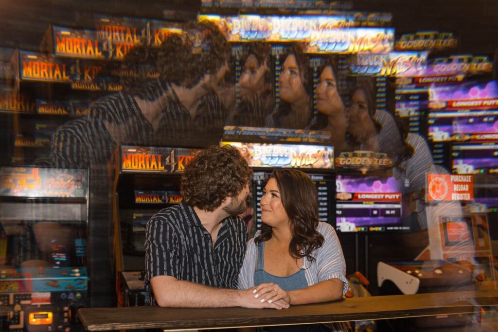 Couple holds hands and looks at one another in front of an arcade with a prism effect.