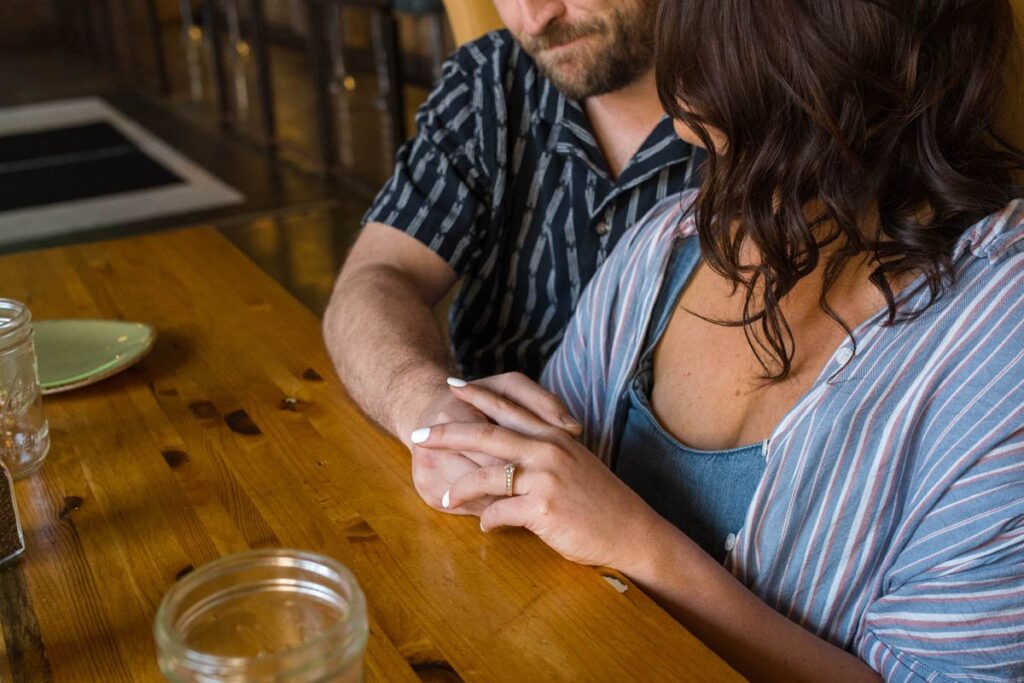 Couple sitting at a table with woman's engagement ring in focus.