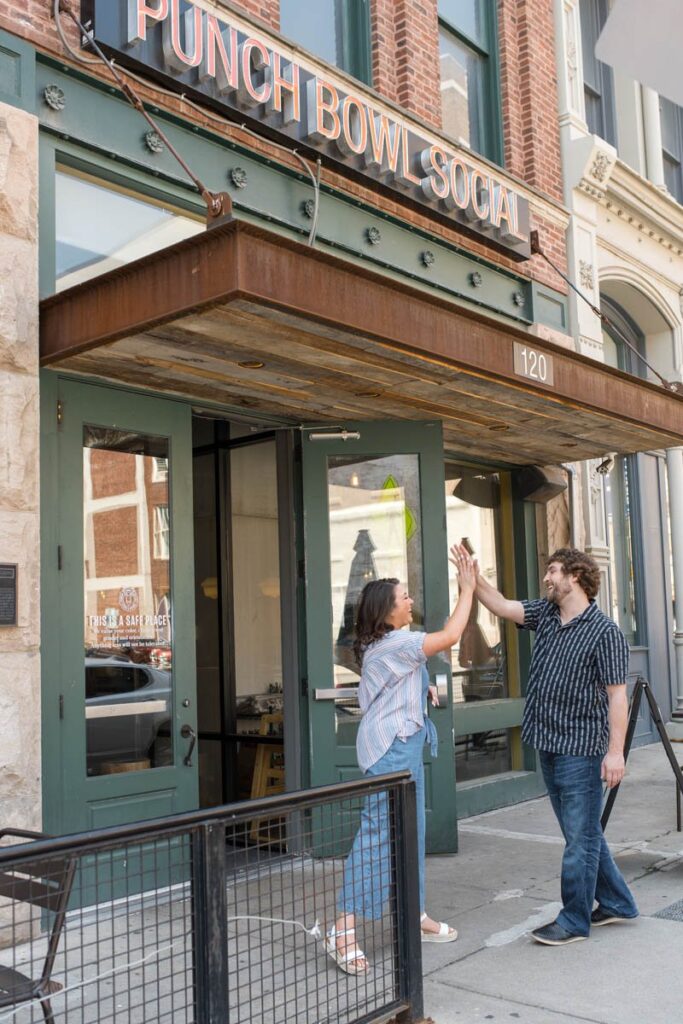Couple laughs and high-fives in front of Punch Bowl Social in Indianapolis.