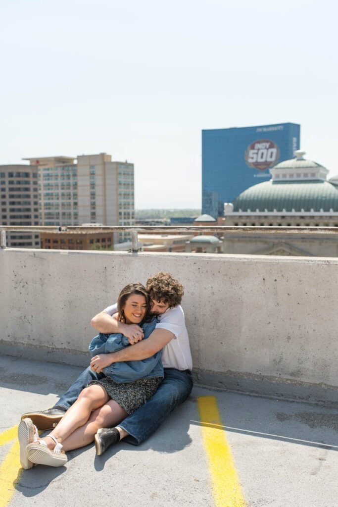 Man hugs woman while sitting together on rooftop parking garage.