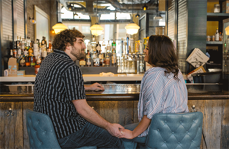 Couple kisses in front of a bar at Punch Bowl Social during their Indianapolis engagement photos.