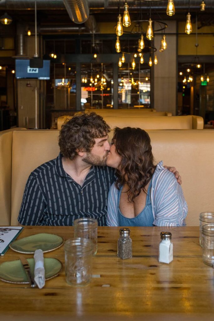 Couple kisses at booth in restaurant.
