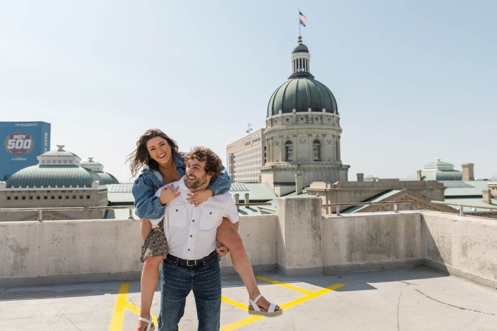 Couple laughs during piggyback ride in front of Indianapolis Capital Building.