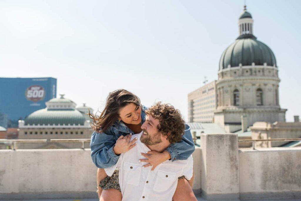Couple looks at each other with Indianapolis State Capital Building behind them during their Indianapolis engagement photos..