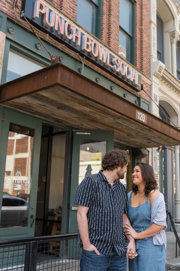 Couple smiles while they look at one another in front of Punch Bowl Social in Indianapolis.