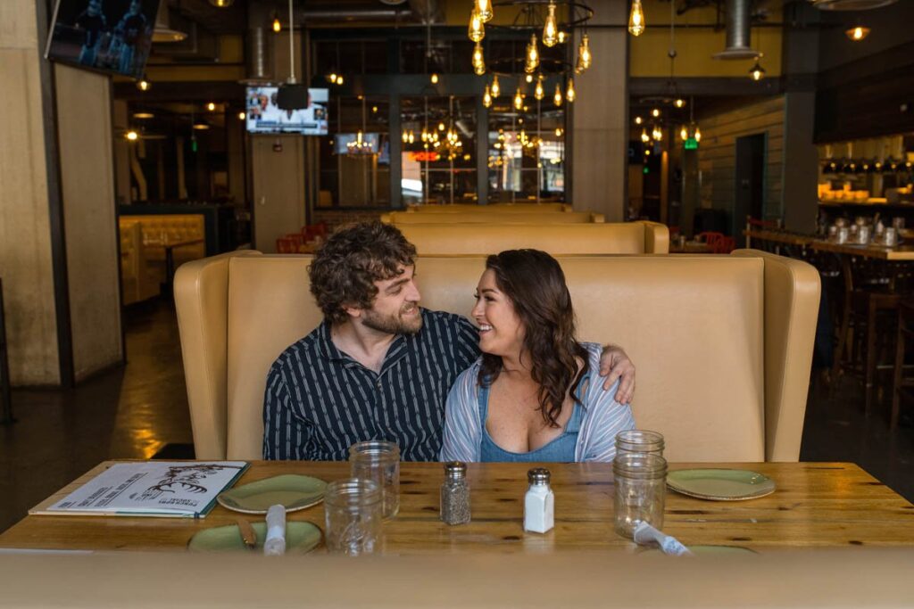 Couple smiles happily as they sit close together in a booth at a restaurant.