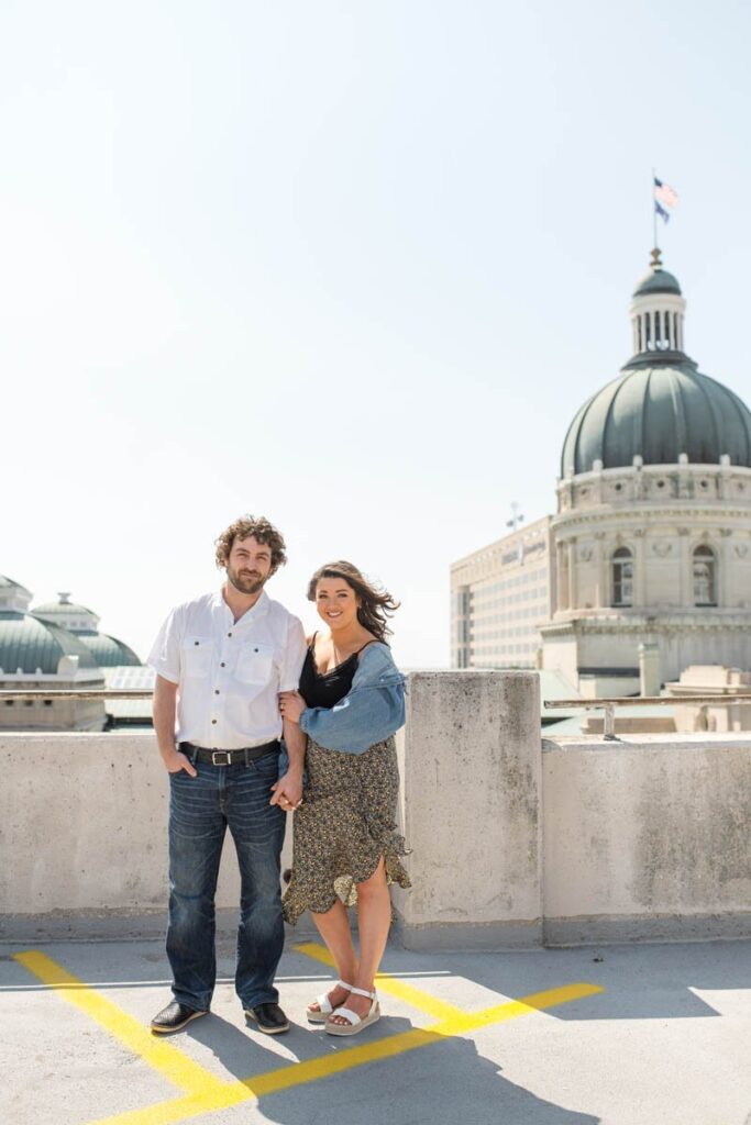 Couple smiles while standing in front of Indianapolis Capital Building for Indianapolis engagement photos.