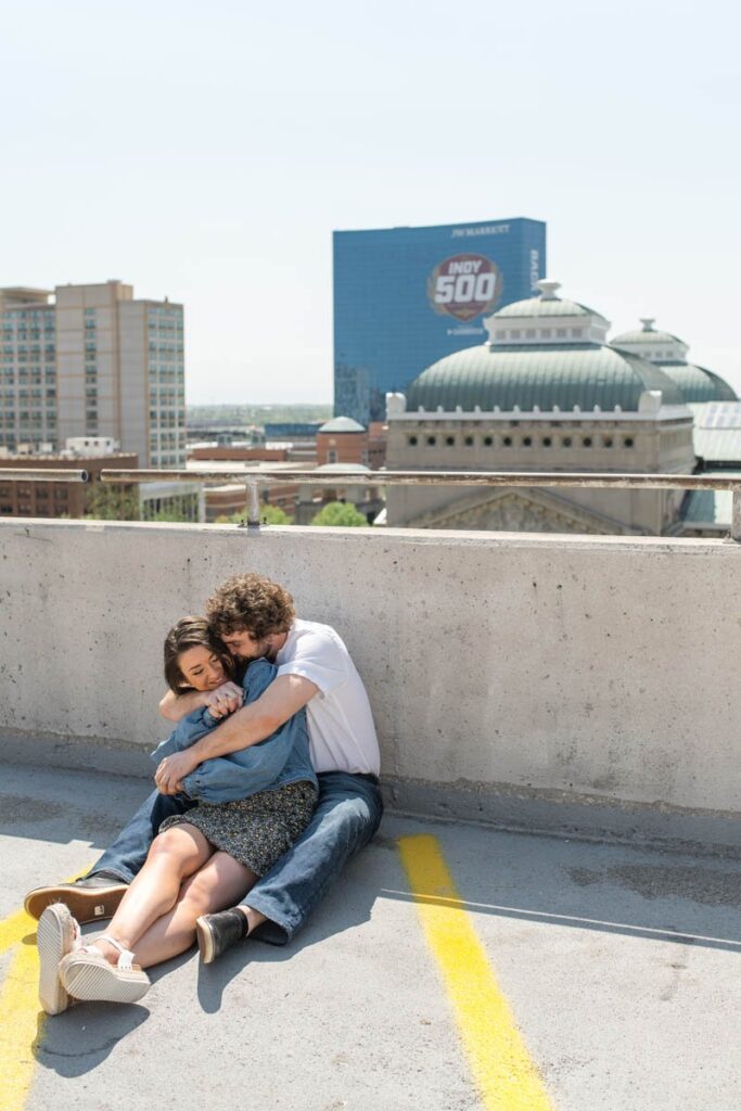 Man and woman in big hug sitting against wall of parking garage.