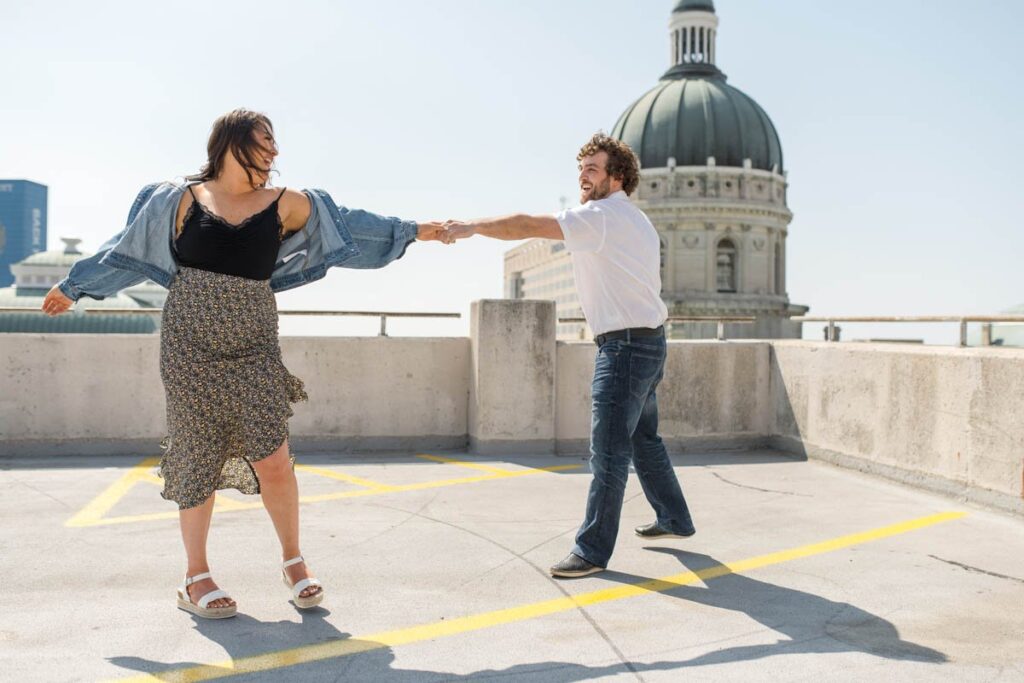 Man spins woman while they dance on rooftop parking garage during their Indianapolis engagement photos.