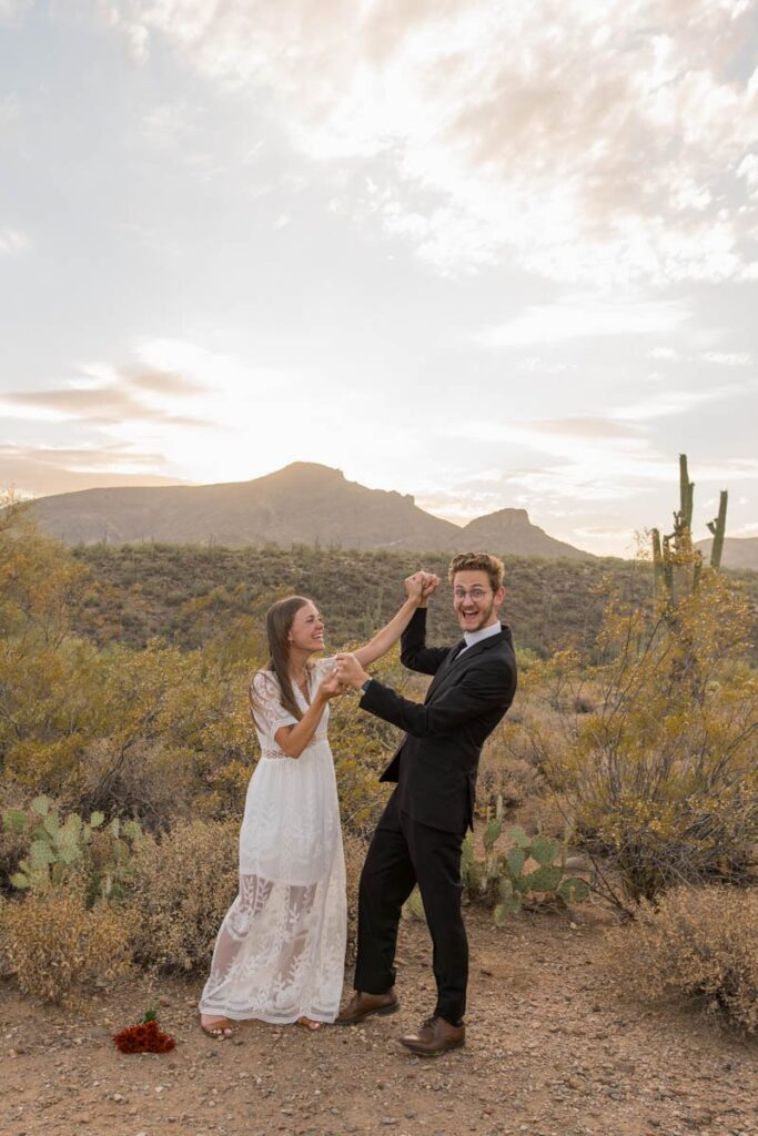 Bride and groom have hands raised and are laughing after eloping in Arizona.