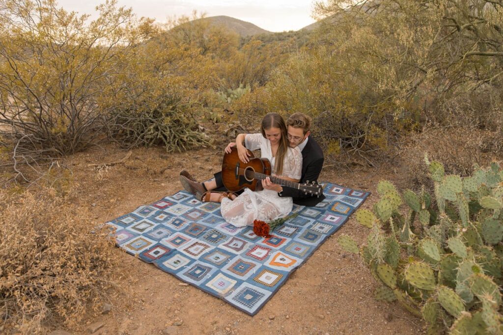 Bride and groom play guitar on a blanket together.