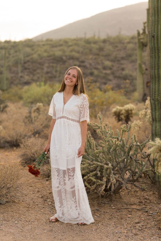 Bride plays with dress in the desert while holding her bouquet of red flowers.
