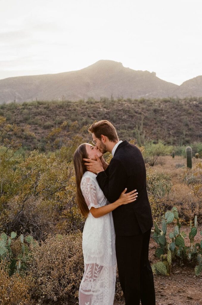 Couple kiss at sunset in front of desert mountains.