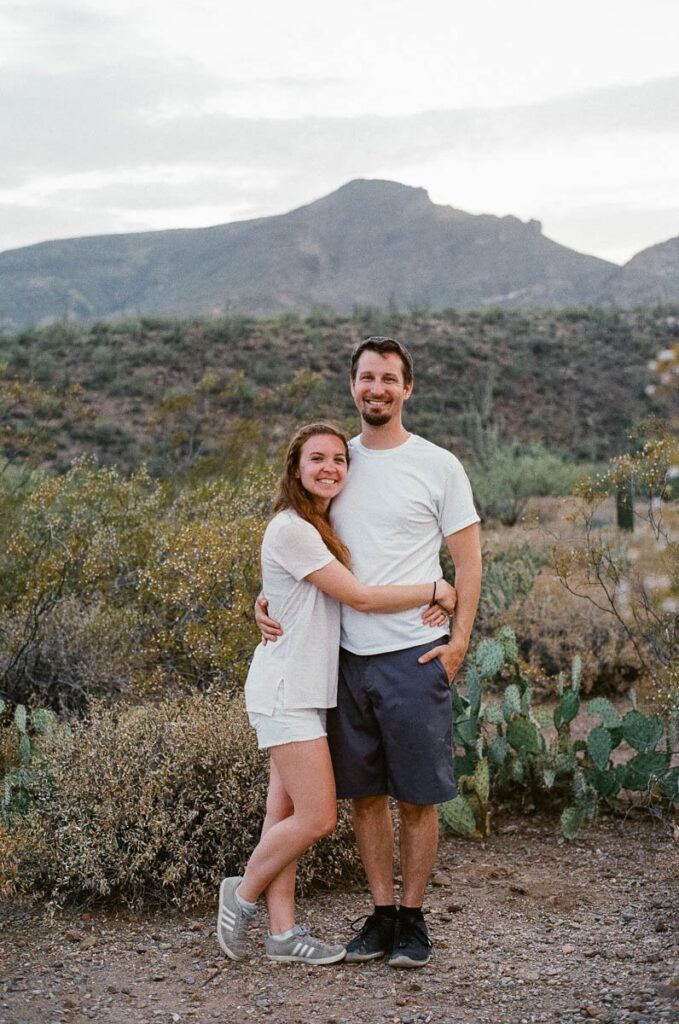 Vallosio Photo + Film Photographers, Jonathan and Ashley, smiling in front of desert mountain.
