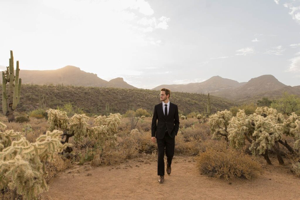 Groom walks in the desert with one hand in his pocket.